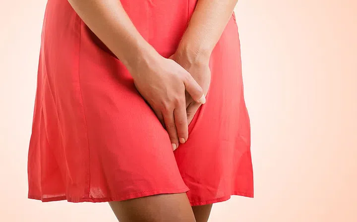 Close up of a woman with hands holding her crotch, isolated in a pink background