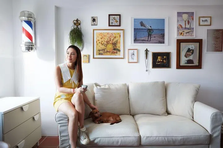Relaxing in the guest bedroom with her dachshund, Billie, named after singer Billie Holiday. In the background, a wall collage embodies feminine energy, featuring, among others, a cherished photo of Phillips’ late mother. Phillips wears an & Other Stories romper and Converse sneakers.Photo: Gan