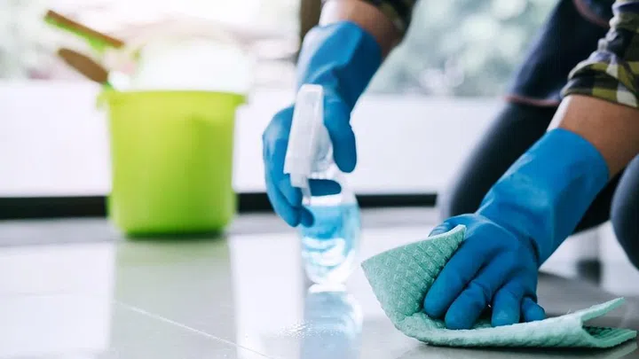 Husband housekeeping and cleaning concept, Happy young man in blue rubber gloves wiping dust using a spray and a duster while cleaning on floor at home.