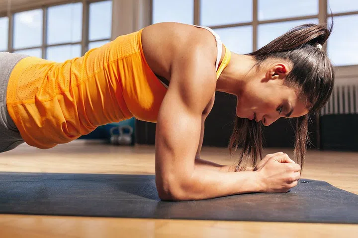 Side view of attractive young woman doing core exercise on fitness mat in the gym. Female doing press-ups in health club.