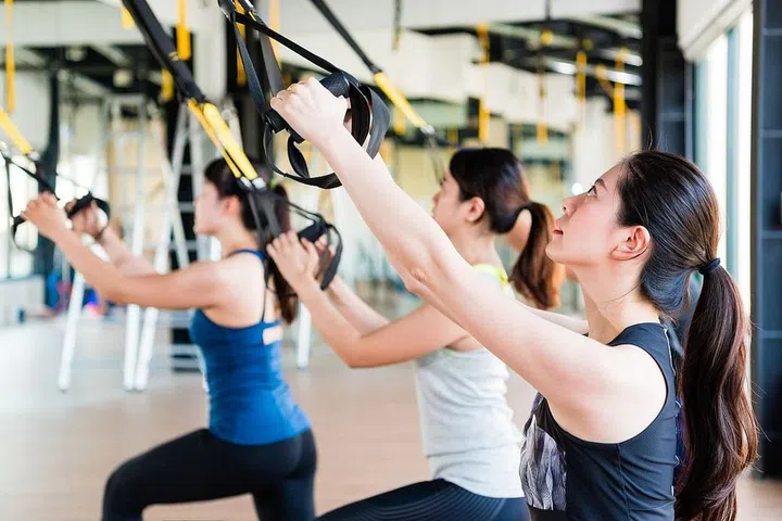 beautiful Asian girl learning using total body resistance exercise TRX for training her slim body pull and look up.