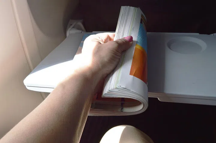 Woman sitting at the window in the plane and leafing through the magazine.