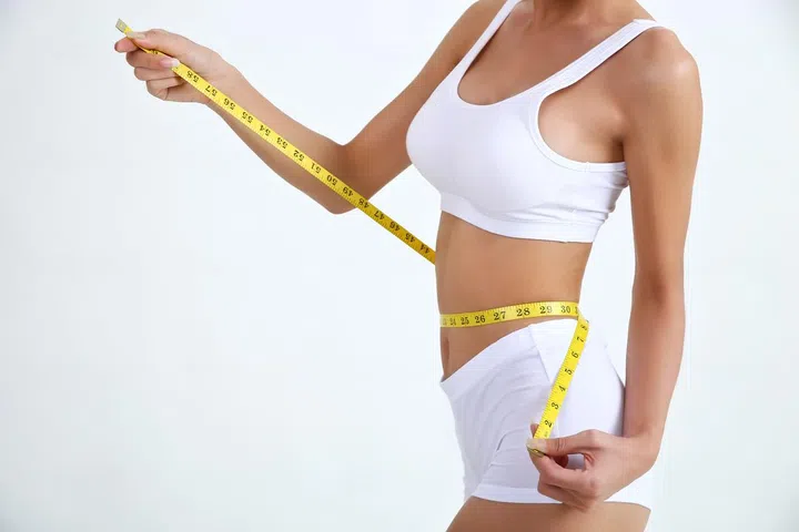 Close up slimming female with beautiful body and measuring her waistline  with measure tape on white background and copy space