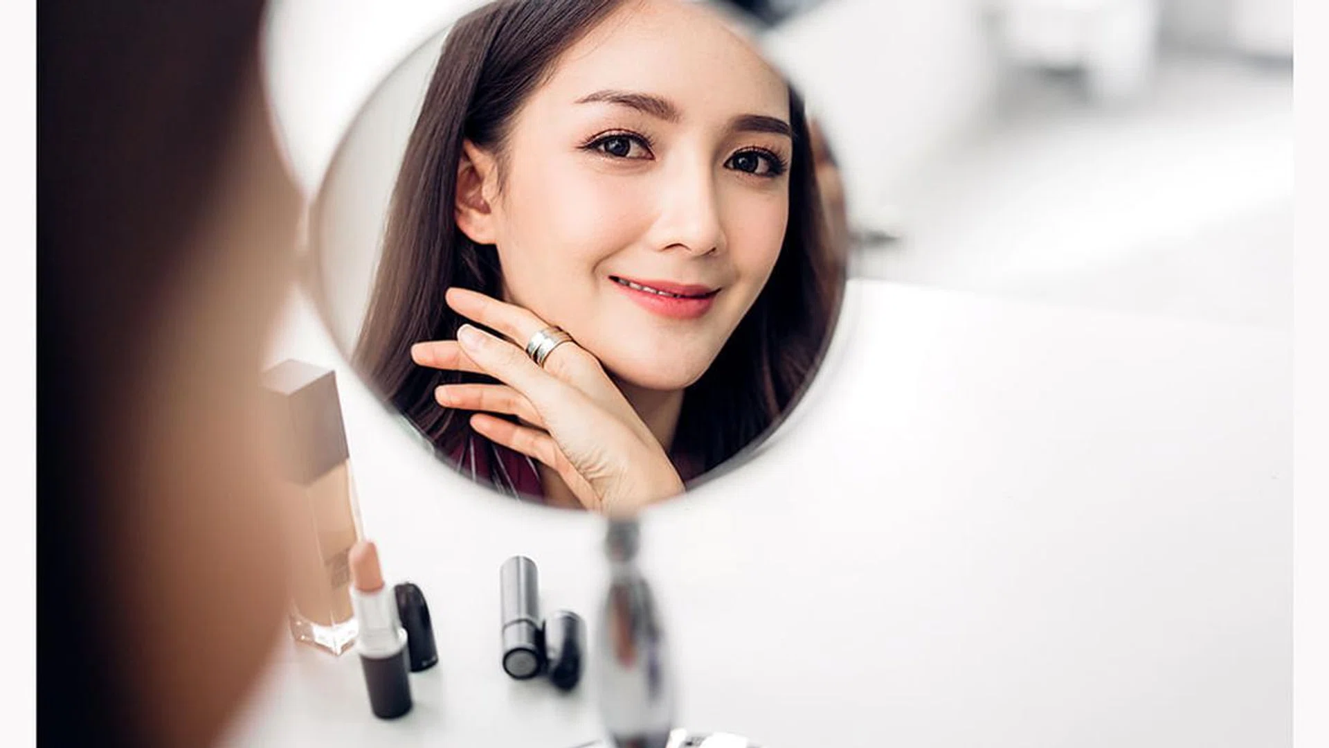 Smiling young beautiful woman fresh healthy skin looking on mirror with makeup cosmetics set at home.facial beauty and cosmetic concept