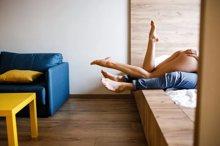 Young sexy couple have intimacy on bed. Well-built and slim woman lying on man. Her legs posing. Man's hand on her buttocks. Together
