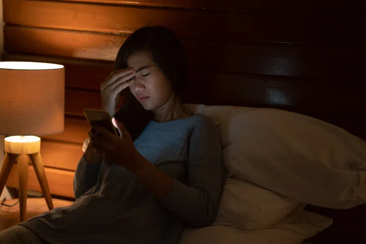 frustrated upset woman lying in bed looking at smart phone at night