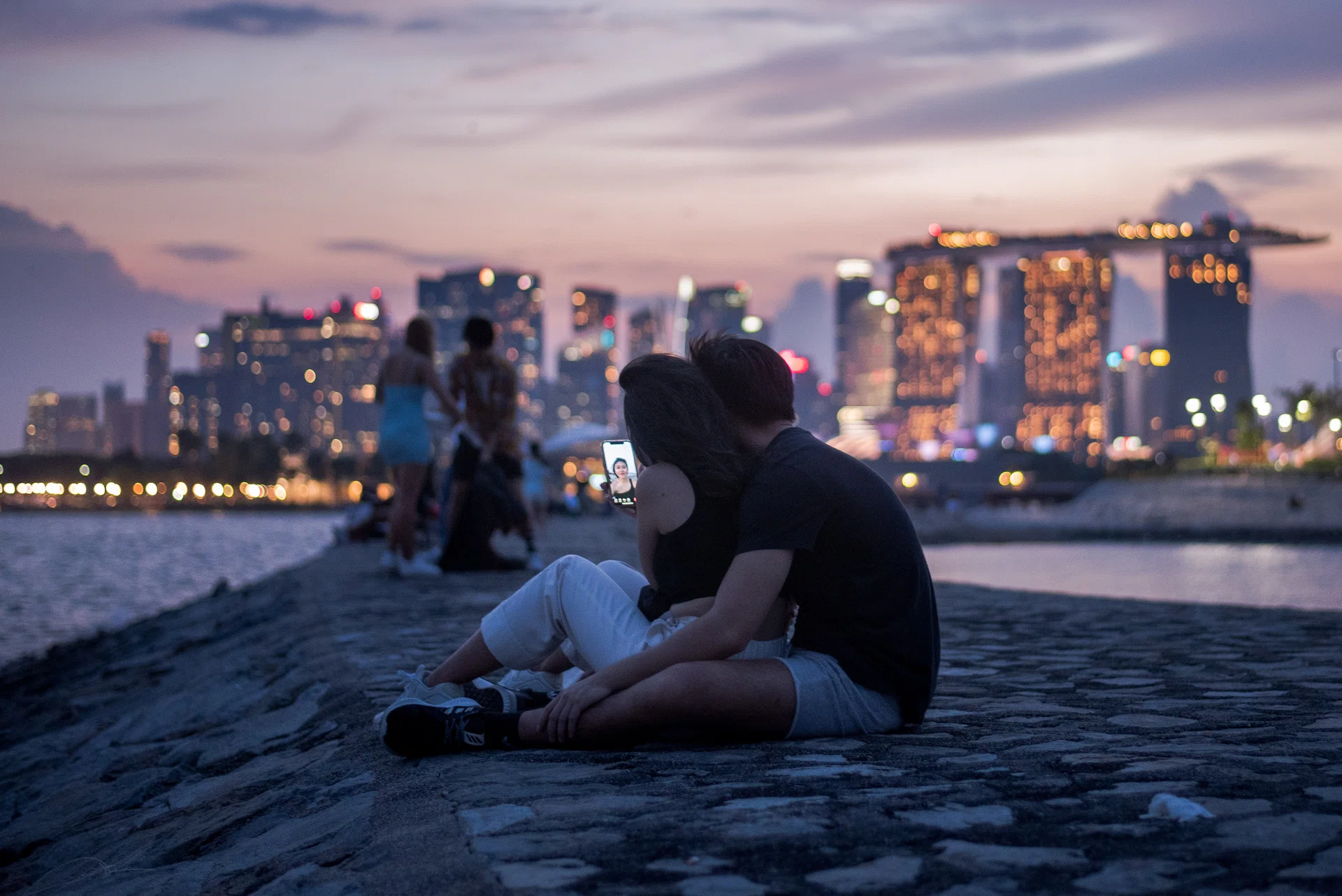 A couple sit on a breakwater with a view of the city skyline in the Marina Bay area of Singapore  on 6 June 2021. Singapore is in the final week of social restrictions that end on June 13 that were enacted after a spike of local COVID-19 cases. Among the restrictions are limits on social interaction disallowing groups larger than two, encouraging residents to keep within their households. (Photo by Joseph Nair/NurPhoto via Getty Images)