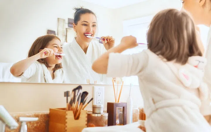 Happy family! Mother and daughter child girl are brushing teeth toothbrushes in the bathroom.