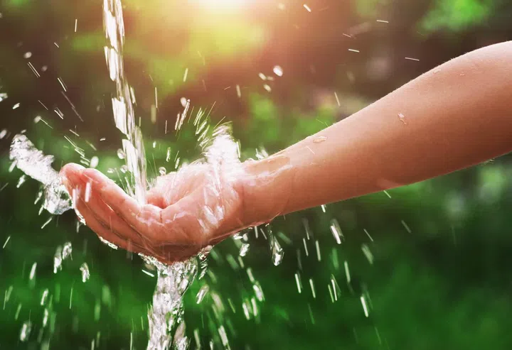 Water pouring splash in hand and nature background with sunshine