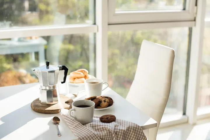Early morning french home breakfast, coffee and cookies on the table near window in bright sunlight, white interior
