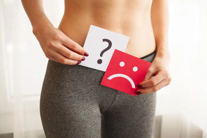 Vaginal or urinary infection and problems concept. Young woman holds paper with sad smile above crotch.