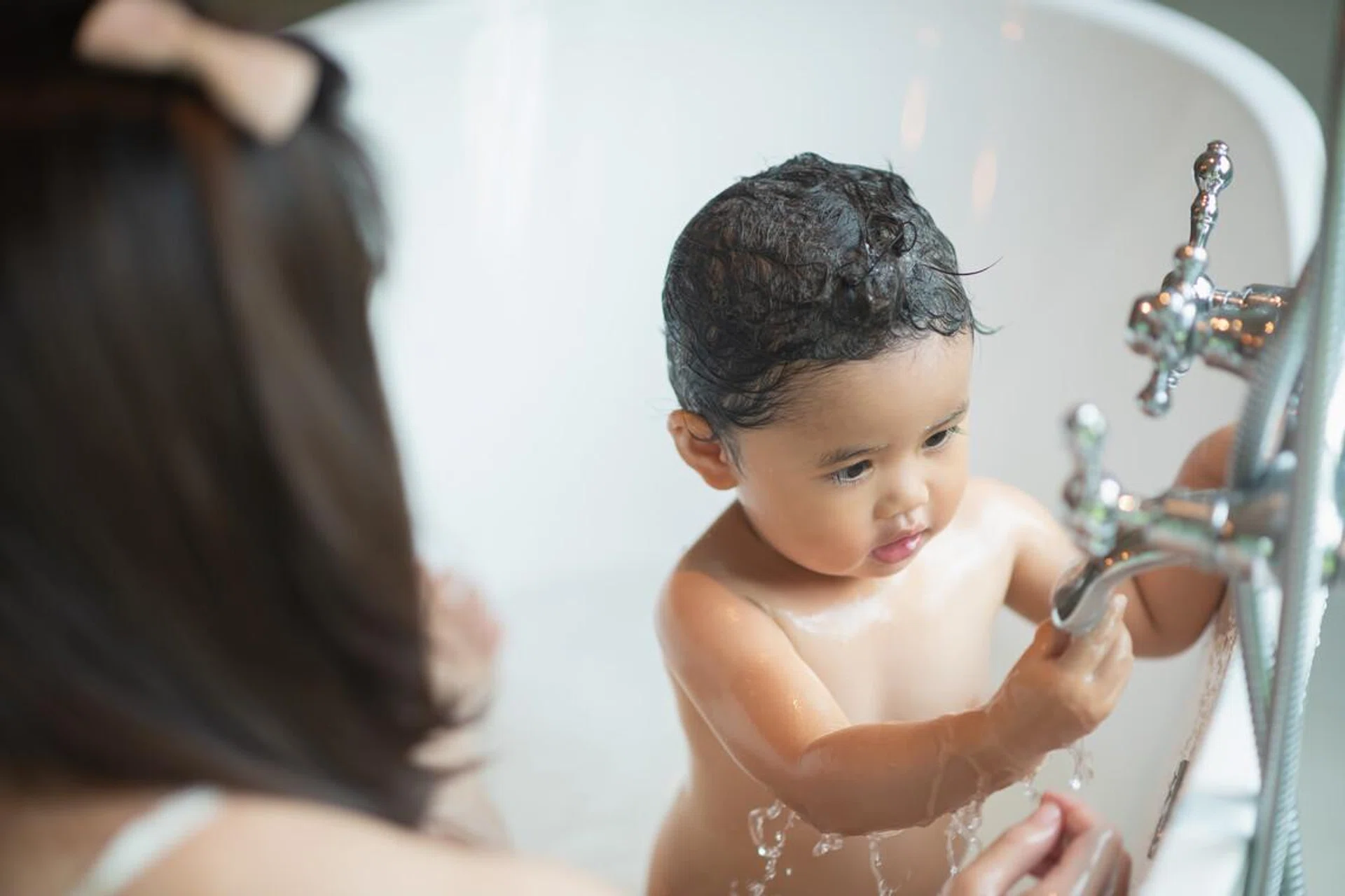 Cute baby taking a shower in bathtub.
