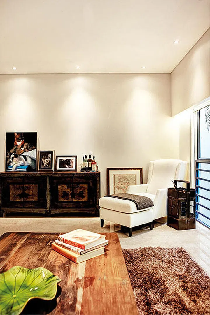 A cosy and well-lit reading corner is created right opposite the bookshelf by tucking a cream upholstered armchair and ottoman to the side of the living room and positioned under downlights. 