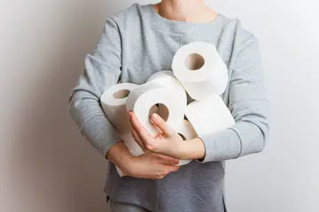 Woman stretches forward many rolls of toilet paper. Close-up without a face, studio, white background.