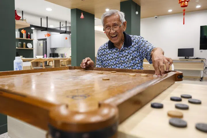 Mr Lam Shaw Ying, 88, retired school supplier, playing carrom at the Good Old Place, the elderly activity centre in Harmony Village @ Bukit Batok on Jan 7, 2025. Previously living in a private housing in Katong, he moved into Harmony Village with his wife more than a month ago. 