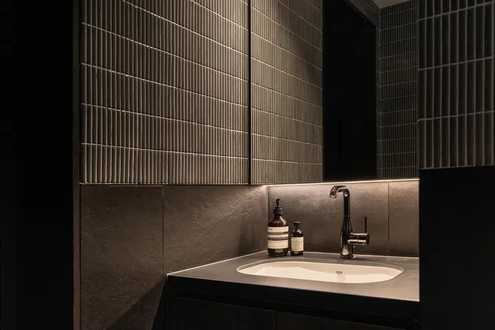The common bathroom adopts a darker, more masculine palette—a deliberate departure from the rest of the home that reflects Anthony’s preference while standing up well to frequent use by guests.