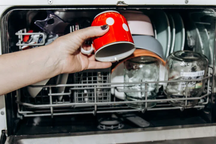 Female hand lays the dishes in an open dishwasher close-up clogged with clean, washed dishes. dry cutlery closeup. spoons forks. mugs, plates. household appliances in the kitchen.