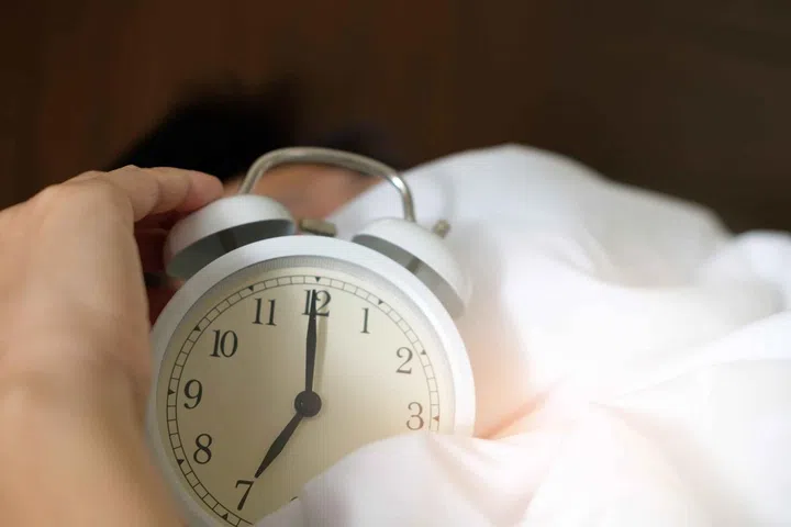 How to Sleep Better? An Ear Nose Throat Doctor Shares Expert Tips. Person holding clock in bed