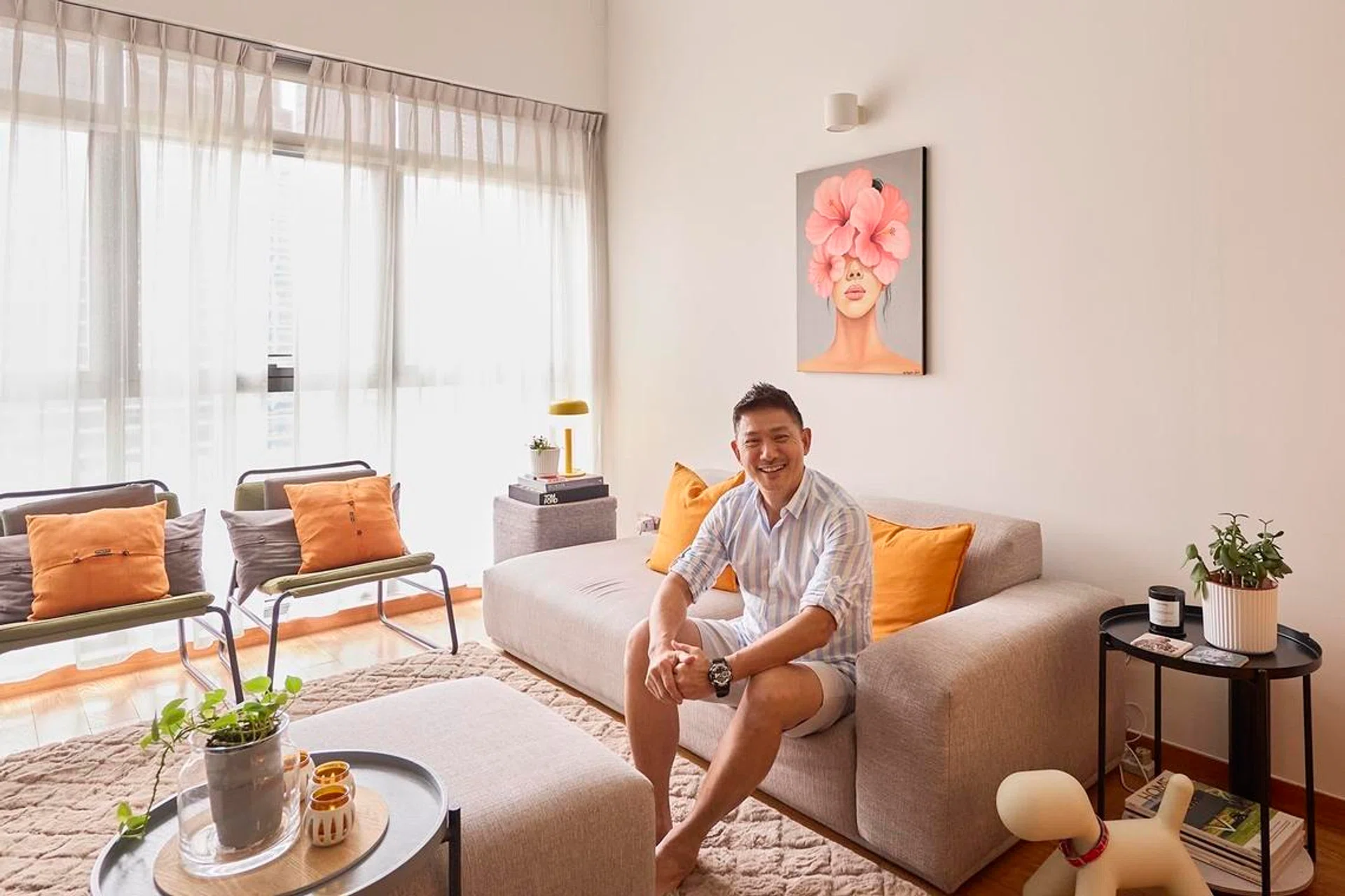 Terence in the double-volume living room, where tall windows flood the loft with daylight and warm orange accents reflect his signature colour palette.