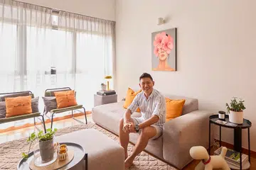 Terence in the double-volume living room, where tall windows flood the loft with daylight and warm orange accents reflect his signature colour palette.
