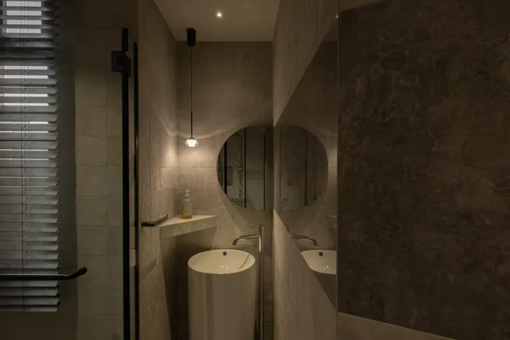 A horizontal band of reflective tiles meets an angled mirror at the basin, layering light and reflection across the compact space.