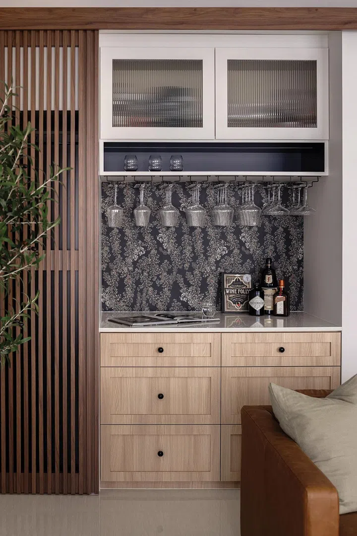 A compact bar area beside the wine fridge offers plenty of storage space. Custom wallpaper adds flair to the space.