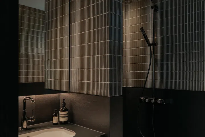 Dark ribbed tiles and black fittings give the guest bathroom a distinctive identity, while complementing the adjoining dark timber finishes throughout the communal spaces.