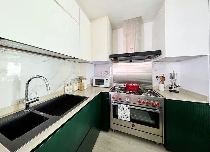 Pine green kitchen cabinets paired with a marble backsplash and stainless steel fire gas stove and hood.