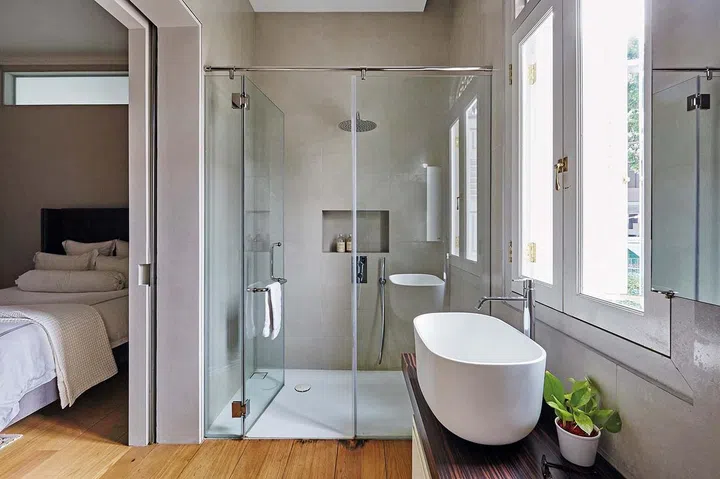 This ensuite bathroom has a clear glass wall, making the whole room feel larger and inviting.