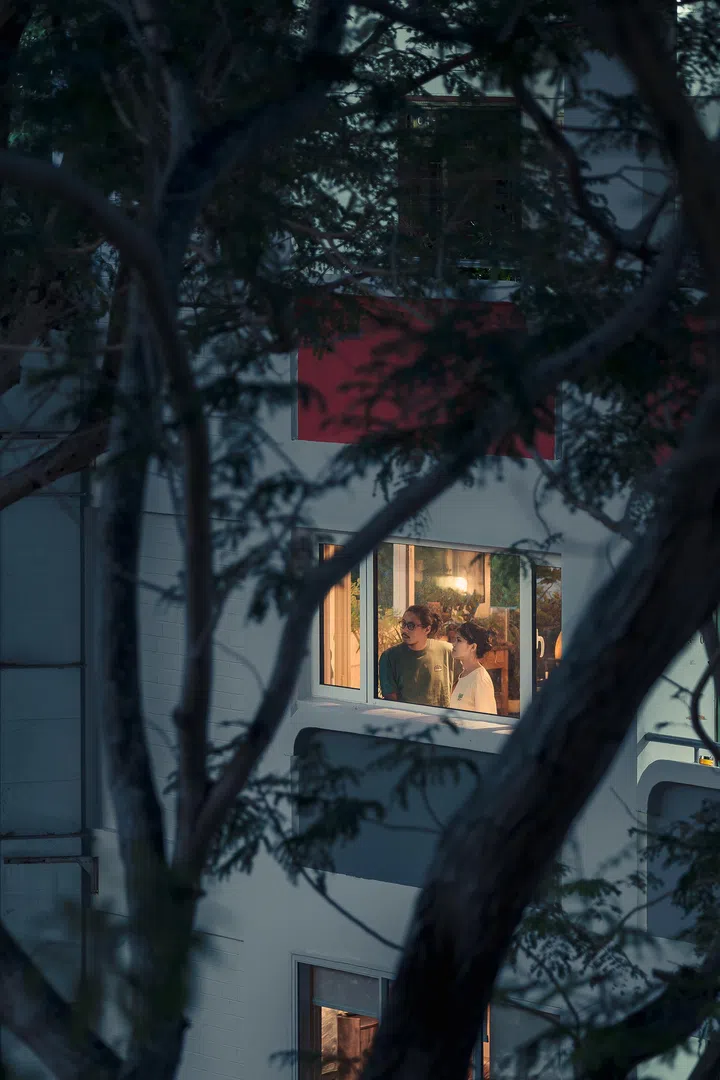 Framed by trees, the couple look out from their Geylang East flat — a home redefined by acute geometry, trust, and years of friendship.