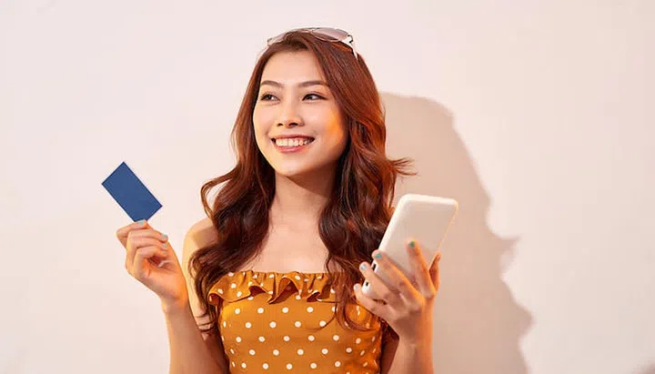 Portrait of a happy girl holding mobile phone and a credit card isolated over biege background