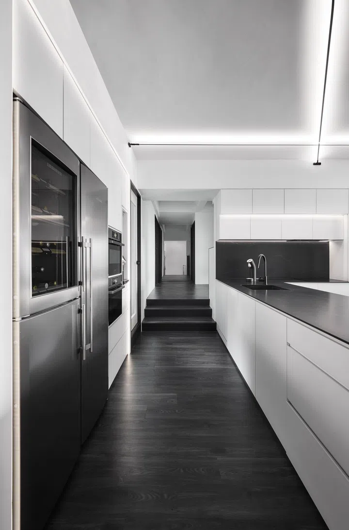 The extended corridor, lined with clean cabinetry and graphic lines, separates communal and private zones while reinforcing the home’s monochrome geometry.
