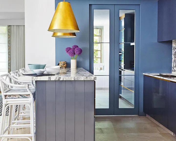 The design of the dry kitchen incorporates Arabescato marble countertops and blue and grey laminates. Large pendant lamps in brass anchor the space.