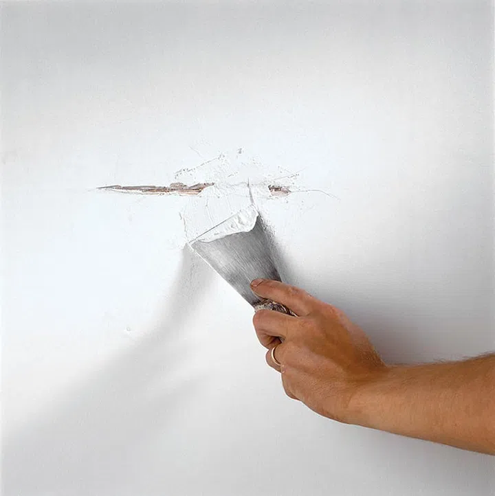 Man concealing and repairing a wall crack with caulking compound or putty and a putty knife.