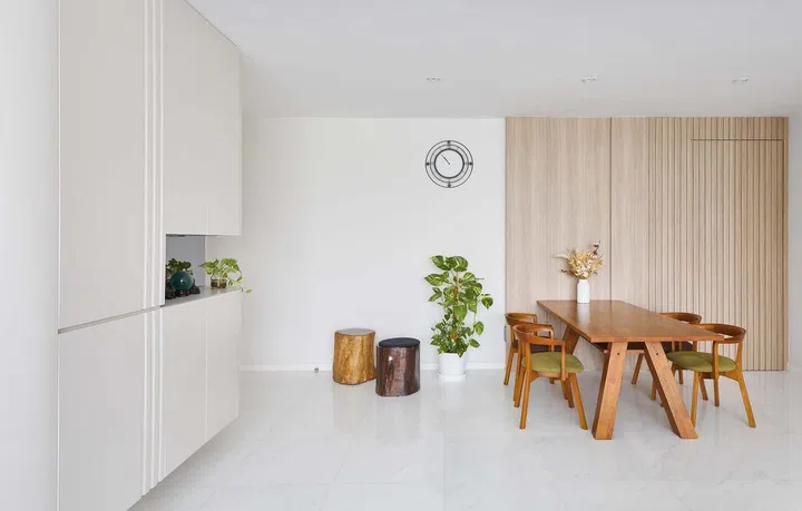 An all-white and wood dining area for a couple in their 60s and their son lives in this 1,550 sqft 3-bedroom condominium apartment in Keppel Bay. Interior design by Weiken.