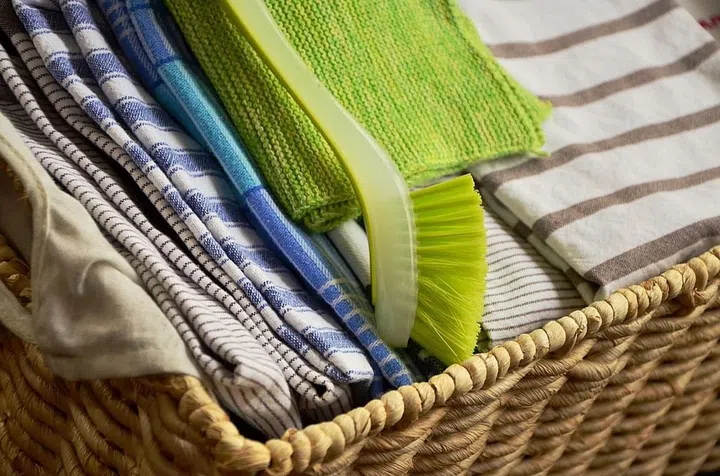 Rattan basket full of folded kitchen towels in assorted cool colours of blue, green brown