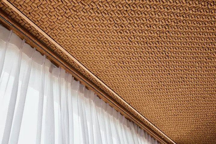Wine cork panels form part of a layered ceiling system, paired with rock wool insulation to reduce heat gain from the roof and dampen noise from rain on the polycarbonate awning above.