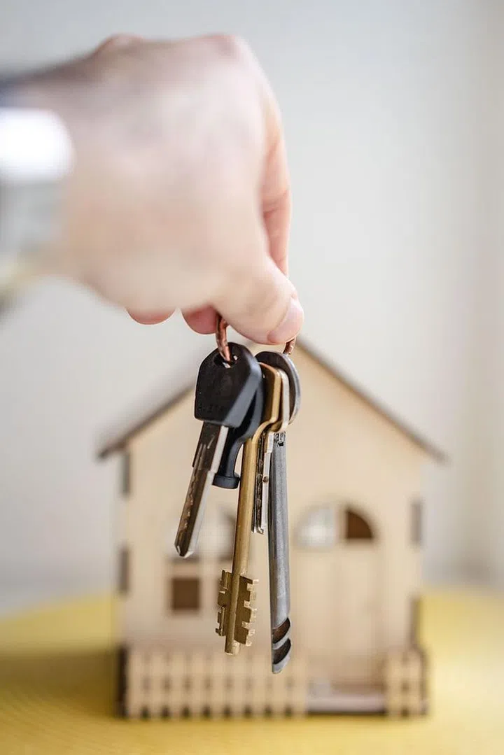 A hand holding a set of keys against a house model