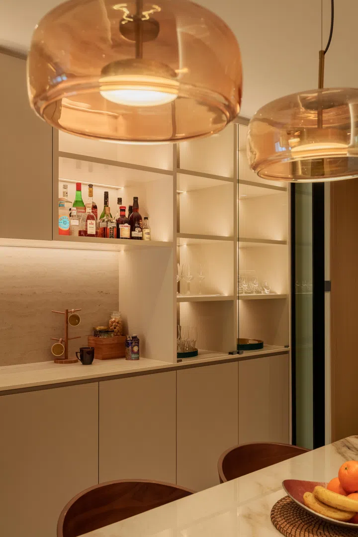 Amber-toned pendant lights and softly backlit cabinetry lend the dining space a warmer, more hospitality-inspired atmosphere.
