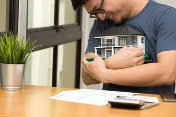 Asian man smiling and hugging a dream home and calculate to buy a house dreaming at his future, Happy and real estate concept.