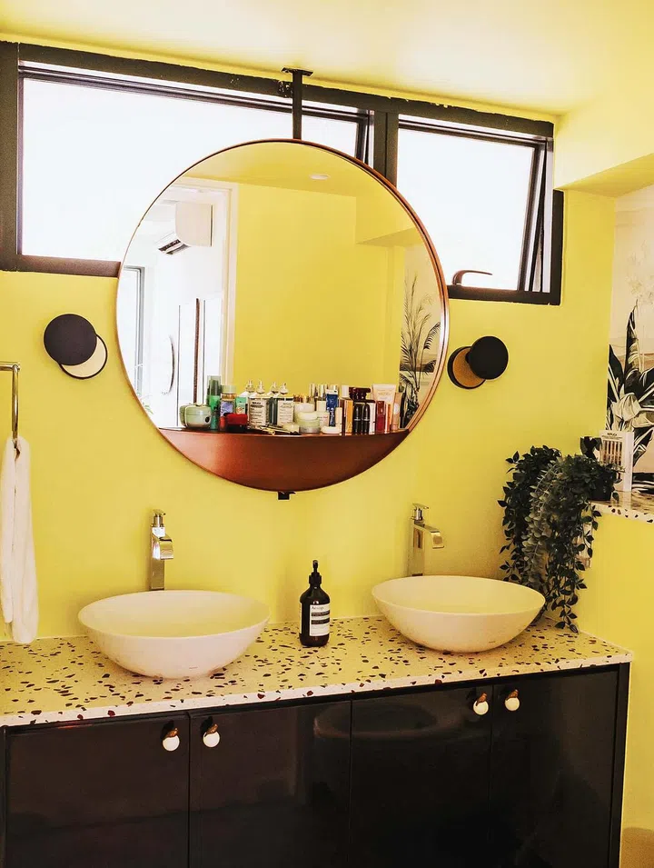 The powder room features pigeon knobs, brown terracotta- like floor tiles, a terrazzo countertop and a double vanity. Notable here is the mirror, modified with a hanging rod so that it can be placed in front of the windows.