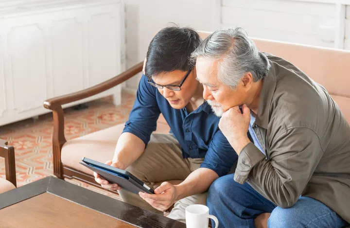 Happy senior asian father and adult son using tablet smartphone in living room