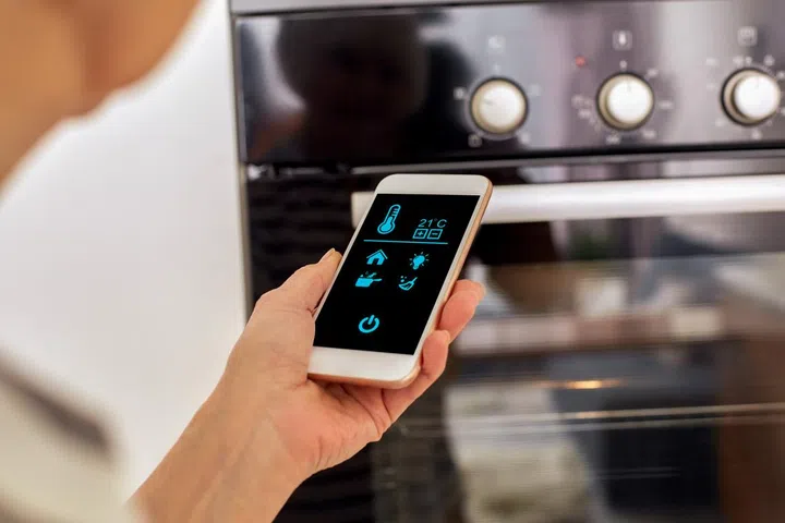 In a modern kitchen, a hand reaches for a sleek smartphone displaying temperature controls.