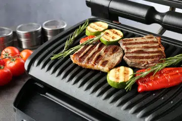 Electric grill with beef steaks, vegetables and rosemary on gray table, closeup