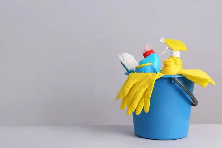 A blue bucket filled with cleaning gloves, tools, and detergent bottles