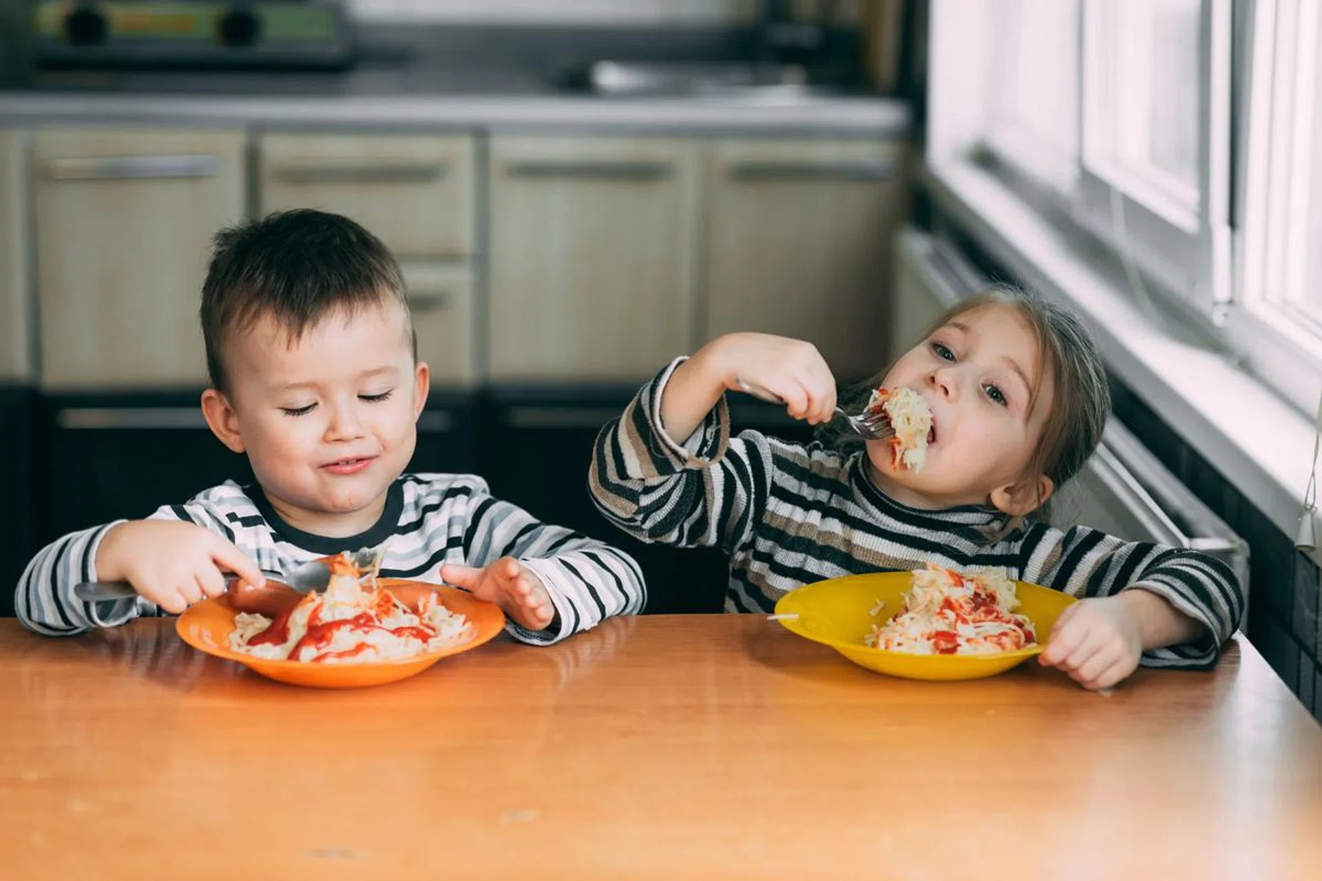 Boy and girl in the kitchen eating pasta. Photo 123RF