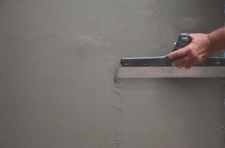 Hands of an old manual worker with wall plastering tools renovating house. Plasterer renovating outdoor walls and corners with spatula and plaster. Wall insulation. Construction finishing works. Image from 123RF