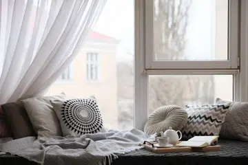 Comfortable lounge area with blanket and soft pillows near window in room. Photo 123RF