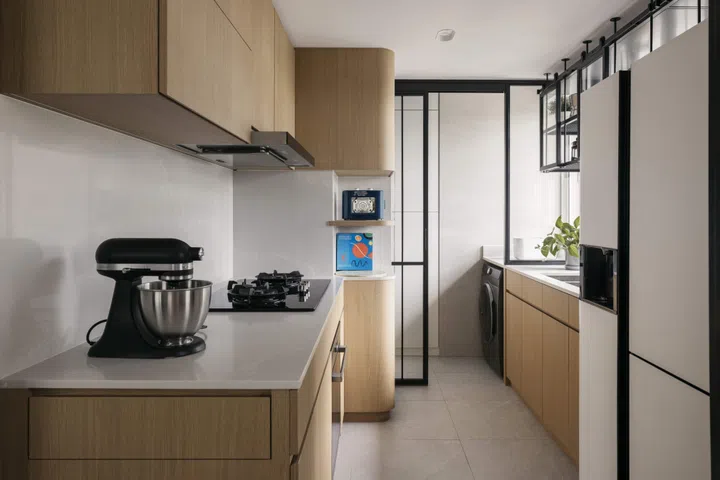 Light-toned cabinetry and glass-backed shelving keep the kitchen open and visually connected, while a pull-out counter supports family activities.