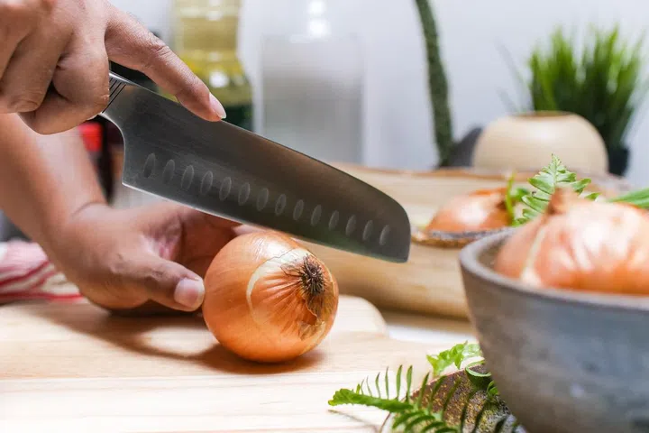 Close up of woman hands cutting onion on wooden cutting board in kitchen